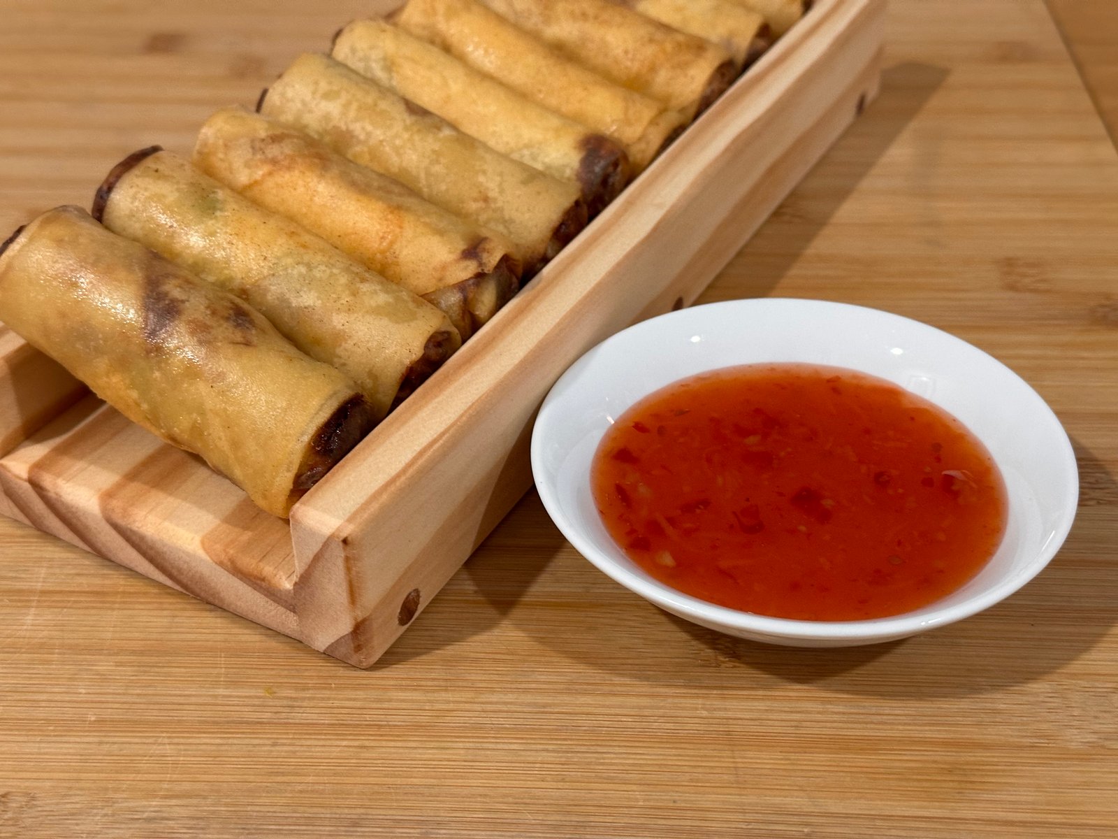 Close view of spring rolls resting on the wooden guide beside dipping sauce