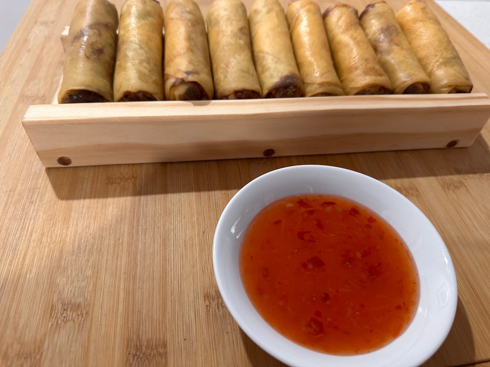 Front view of spring rolls on the wooden guide with dipping sauce in the foreground