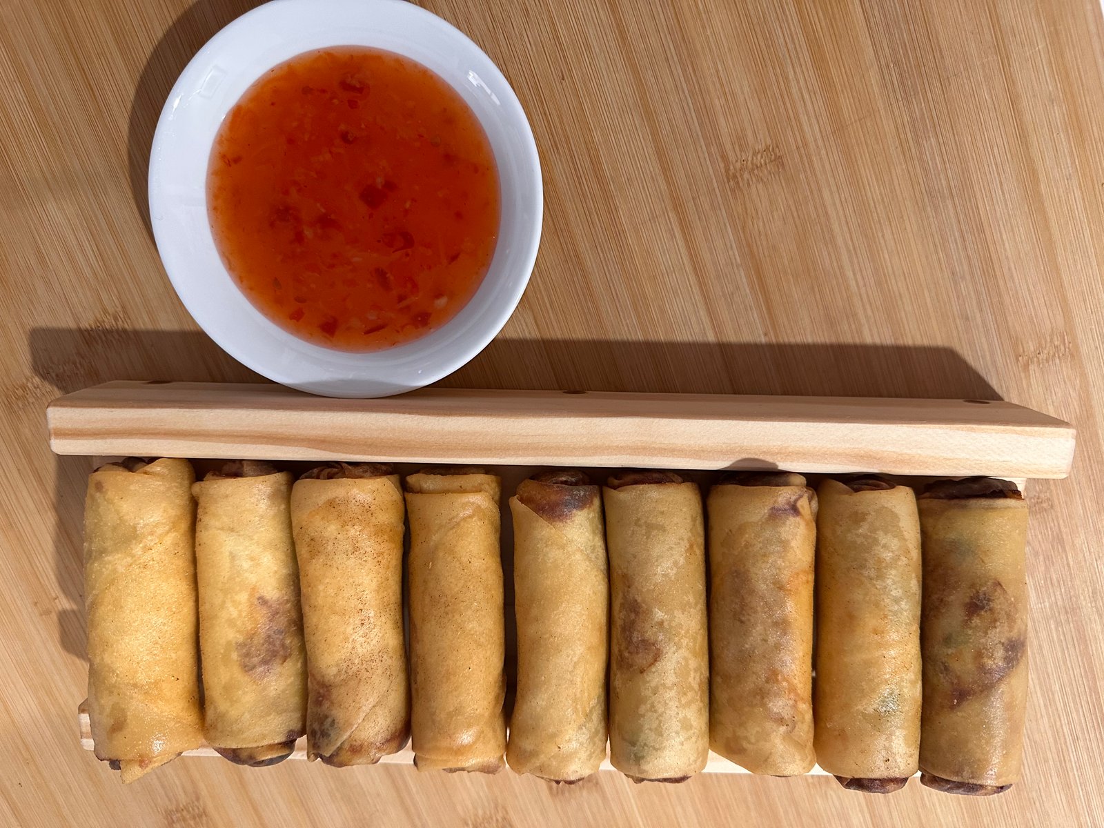 Overhead view of spring rolls lined up across the wooden guide