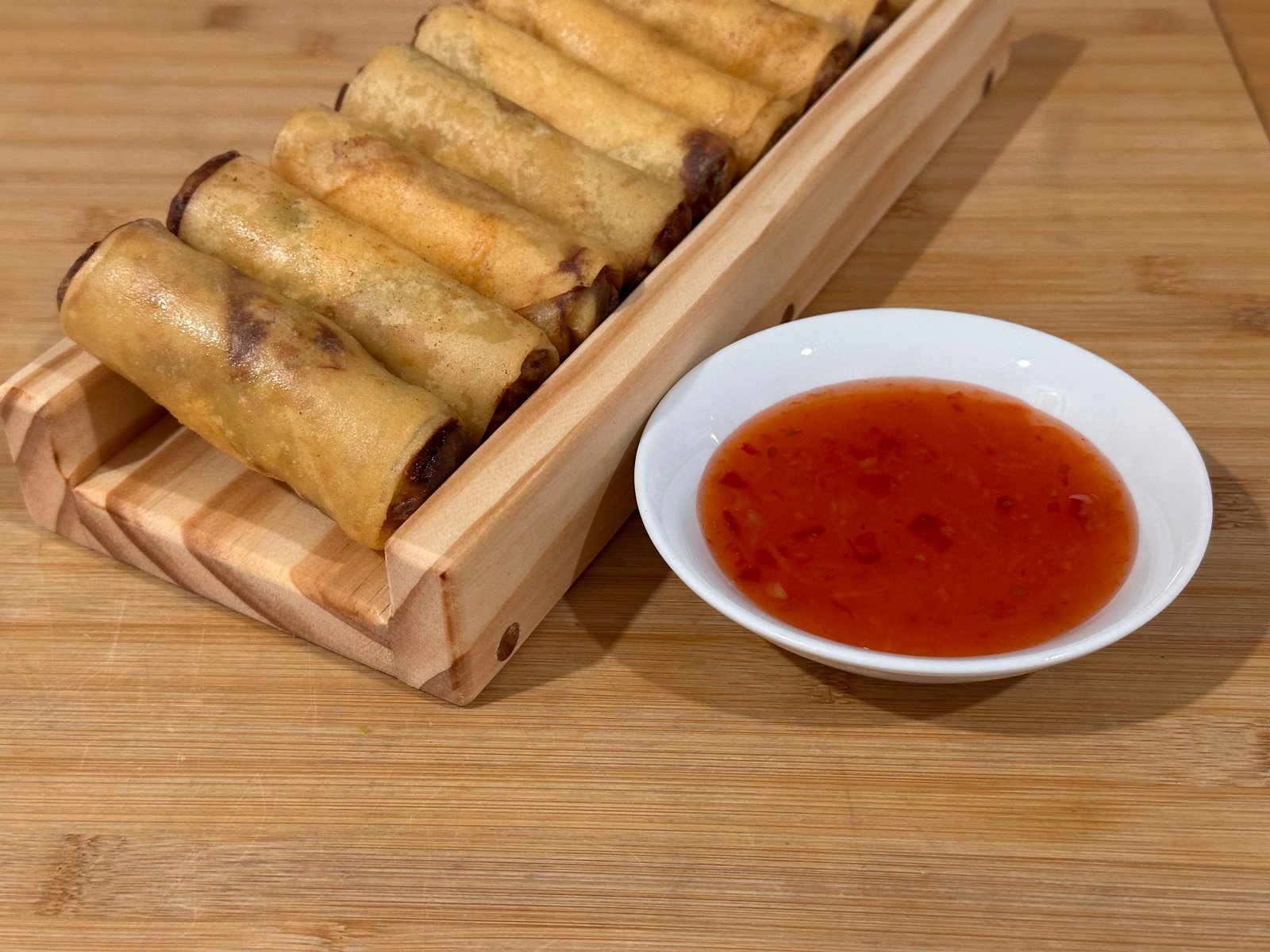 Golden spring rolls arranged on SpringRollPro beside a bowl of dipping sauce